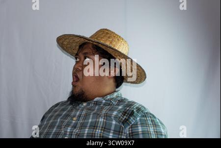 Ein indonesischer Mann trägt einen Strohhut und ein grünes kariertes Hemd auf weißem Hintergrund. Stockfoto