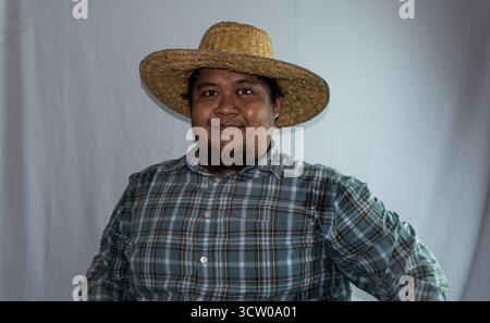 Ein indonesischer Mann trägt einen Strohhut und ein grünes kariertes Hemd auf weißem Hintergrund. Stockfoto