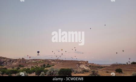 Das weltberühmte Spektakel von Dutzenden Heißluftballons, die während des Sonnenaufgangs friedlich über die einzigartige Landschaft von Göreme in Kappadokien, Türkei, schweben Stockfoto