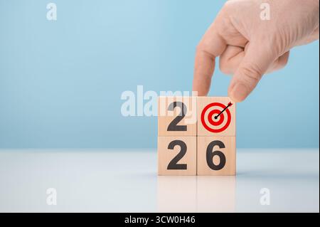 Männliche Hand, die Holzwürfel mit 2026 Zahlen und Zielsymbol anordnet. Konzept für neue Geschäftsvision, Ziele und Planung Stockfoto