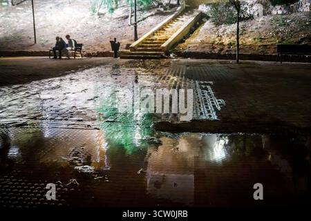 Aus nächster Nähe ein Blick auf einen nassen Kopfsteinpflasterplatz in Villajoyosa mit einer großen Pfütze, die die hellen Lichter und Farben des Ar reflektiert Stockfoto