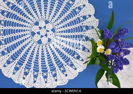 Großes, rundes, regionales, gehäkeltes Deckchen auf dunkelblauem Hintergrund mit blauen und weißen Blüten. Stockfoto