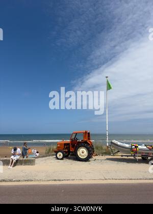 25. JUL 2025 - Normandie, Frankreich - Ein Strand in der Normandie mit einem roten Traktor geparkt, der darauf wartet, Boote vom langen Sandstrand aus zu holen Stockfoto