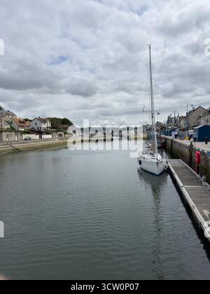22. JUL 2025 - Port-en-Bessin-Huppain, Normandie, Frankreich - das Hafengebiet mit Kanal und Booten, das auf das Meer hinausgeht, in diesem malerischen Dorf der Normandie. Stockfoto