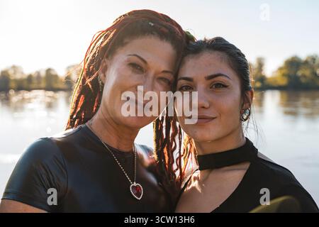 Zwei Frauen mit Dreadlocks stehen nahe und teilen sich einen Moment der Zuneigung am See Stockfoto