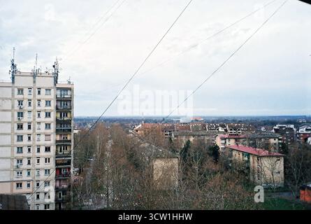Analoges Foto von einem Balkon eines Gebäudes aus der sozialistischen Ära mit Blick auf ähnliche gelbe Backsteingebäude. Bedeckter Himmel. Dokumentarische Stadtarchitektur Stockfoto