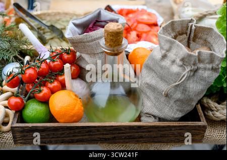 Holztablett mit frischem Zitrusgemüse und einer Flasche Kochöl. Stillleben mit Kirschtomaten, Knoblauch und Zitrusfrüchten in rustikalem Stil. Stockfoto