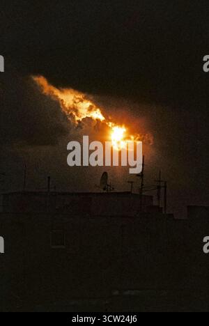 Sonnenuntergang bricht durch dunkle Sturmwolken über Dächern mit Antennen. Atmosphärische und stimmungsvolle urbane Szene, aufgenommen auf analogem 35-mm-Film. Stockfoto