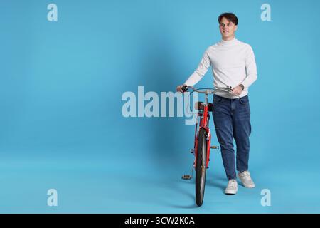 Gutaussehender Mann mit rotem Fahrrad auf hellblauem Hintergrund, Platz für Text Stockfoto