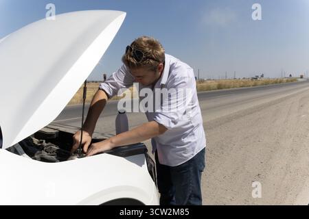 Ein Mann sucht unter der Motorhaube eines Pannenwagens am Straßenrand Stockfoto