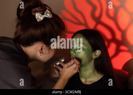 Der Make-up-Künstler eines jungen Mädchens wendet Make-up an, das von einem gruseligen Helden inspiriert wurde Stockfoto
