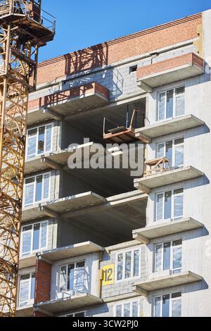 Auf der Baustelle befindet sich ein Wohngebäude mit freiliegenden Böden und Balkonen. Der Kran steht in der Nähe, während sich die Arbeiter auf die Installation und das Fini vorbereiten Stockfoto