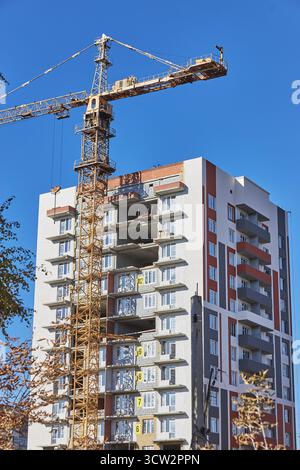Baustelle mit einem hohen Wohngebäude, das fertiggestellt wird. Ein großer Kran ist positioniert, der an sonnigen Tagen ohne Wolken das Material hebt Stockfoto