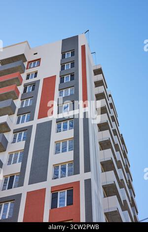 Das hohe Apartmentgebäude besticht durch moderne Architektur mit farbenfrohen Akzenten im Äußeren. Die Struktur steht vor einem hellblauen Himmel und hebt hervor Stockfoto