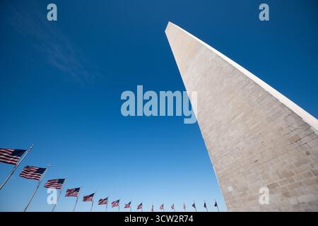 Washington Monument Mit Amerikanischen Flaggen Washington DC | WASHINGTON — Eine Reihe von amerikanischen Flaggen weht im Wind unter dem Washington Monument auf dem National Mall, sein Marmorschacht fängt das volle Sonnenlicht gegen einen klaren Himmel ein. Nach Jahrzehnten unterbrochener Bauzeit 1884 fertiggestellt, erhebt sich der Obelisk 555 Fuß 5⅛ Zoll (169,29 m) und ist damit das höchste Mauerwerk der Welt. Stockfoto