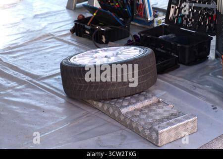 Der flache Performance-Reifen mit weißem Mehrspeichen-Leichtmetallrad liegt auf dem Werkstattboden auf. Stockfoto