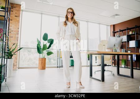 Professionelle Geschäftsfrau steht selbstbewusst in modernen Büroräumen mit stilvoller Einrichtung und eleganter minimalistischer Innenausstattung Stockfoto