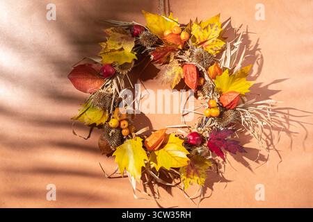 Getrockneter Blumen- und Herbstkranz auf orangefarbenem Hintergrund und abstrakten Schatten. Herbstdekor-Konzept Stockfoto