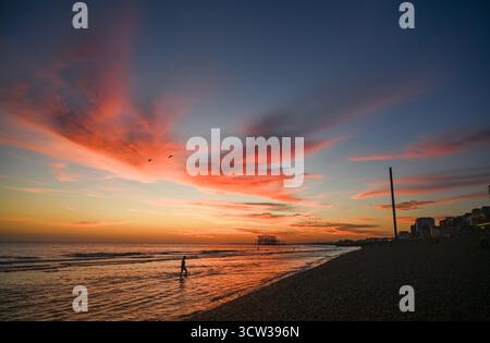 Brighton UK 9. Oktober 2025 - Ein Schwimmer taucht bei Sonnenuntergang über Brighton Beach und dem West Pier nach einem weiteren warmen Tag an der Südküste aus dem Meer auf: Credit Simon Dack / Alamy Live News Stockfoto