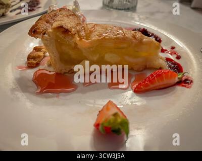 Apfelstrudelscheibe mit Vanilleeis, Erdbeermarmelade und frischer Erdbeere auf einem Teller in Restaurant-Atmosphäre Stockfoto