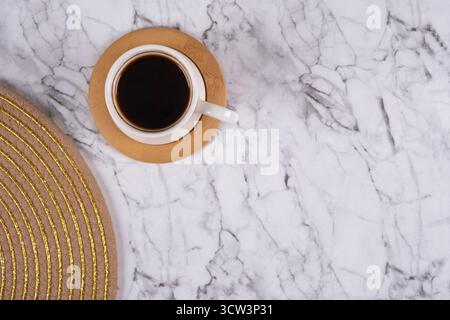 Ein minimalistischer und auffälliger flacher Lay fängt eine Tasse tiefschwarzen Kaffees auf, zentriert auf einem luxuriösen Marmorhintergrund. Dies direkt, an Stockfoto