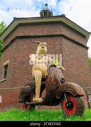 Handgefertigte Korbskulptur eines Comic Grommit Hundes, der auf einem Roller vor dem historischen achteckigen Ziegelkachel auf dem Gelände der lytham Hall reitet Stockfoto