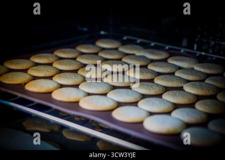 Französische Macarons, die im Ofen auf Silikonplatten backen. Hausgemachtes Dessertzubereitungskonzept. Stockfoto