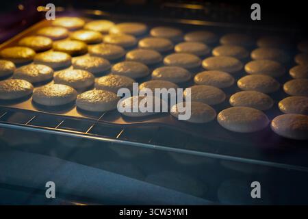 Französische Macarons, die im Ofen auf Silikonplatten backen. Hausgemachtes Dessertzubereitungskonzept. Stockfoto