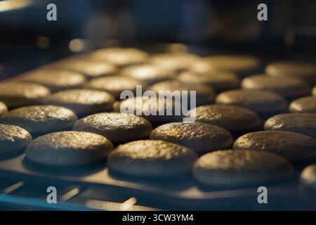 Französische Macarons, die im Ofen auf Silikonplatten backen. Hausgemachtes Dessertzubereitungskonzept. Stockfoto