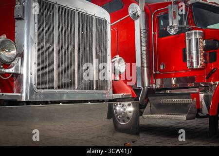 Zwei große klassische rote Lkw stehen nebeneinander auf einer gepflasterten Fläche und zeigen ihre glänzenden Chromdetails bei hellem Sonnenlicht tagsüber. Stockfoto