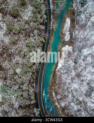 Aus der Vogelperspektive eines pulsierenden blauen Flusses, der sich durch schneebedeckte Wälder entlang einer einsamen Straße schlängelt, Shenandoah, Virginia, USA. Stockfoto