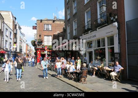 Dublin, Irland - 26. Juni 2015 - Eine lebhafte, geschäftige Szene in der Temple Bar, während die Leute an einem Restaurant mit besetzten Tischen im Freien vorbeilaufen, das das Straßenleben in der irischen Hauptstadt darstellt Stockfoto