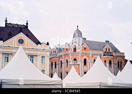Historische Gebäude im alten Zentrum von Novi Sad mit weißen Zelten davor, die in analogem Stil mit sanften Stadttönen gehalten werden. Stockfoto