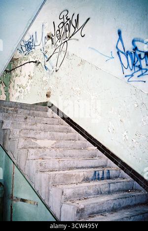 Treppe in einer verlassenen Fabrik ohne Geländer, markiert durch mehrere Graffiti, aufgenommen mit analogem Blitz für einen rauen industriellen Look. Stockfoto