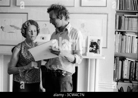 Patrick Procktor Künstler zu Hause in seiner Wohnung in der Manchester Street. Er zeigt seiner Mutter Barbara eines meiner Fotos. Auf dem Mantelstück befindet sich ein Foto von Homer Sykes von Patricks großem Freund Gervase Griffiths, das eine Kopie von Black Dwarf liest. Marylebone, London, England, 1969 1960er Jahre Großbritannien HOMER SYKES Stockfoto