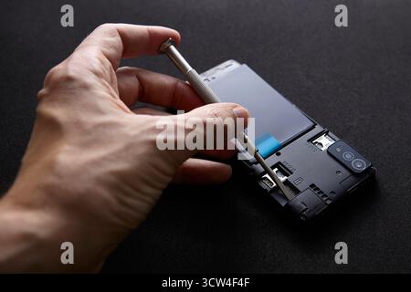 Ein Techniker verwendet einen Schraubendreher, um Smartphone-Komponenten zu fixieren oder wieder zusammenzubauen. Die Abbildung zeigt den technischen Reparaturprozess und die Liebe zum Detail. Stockfoto