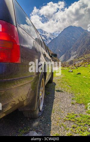 Auto mit Platten Reifen auf Schotterpiste mit Bergen im Hintergrund Stockfoto