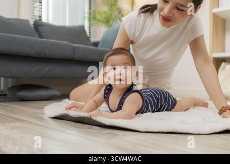 Ein Baby genießt die Bauchzeit auf einer weichen Matte, während die Mutter nah bleibt und es mit einem warmen Lächeln ermutigt. Dieser zärtliche Moment hebt frühe Entwicklungskräfte hervor Stockfoto