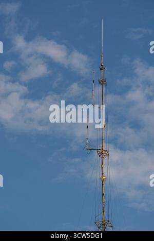 Unter bewölktem Himmel steht ein hoher Funkantennenmast mit gespannten Stützdrähten. Stockfoto