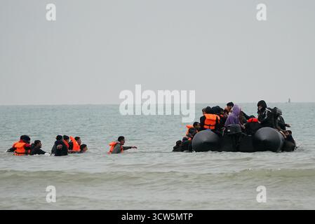 Menschen, die als Migranten gelten, waten ins Meer, um an Bord eines kleinen Bootes in Gravelines, Frankreich, zu gehen. Bilddatum: Freitag, 10. Oktober 2025. Stockfoto