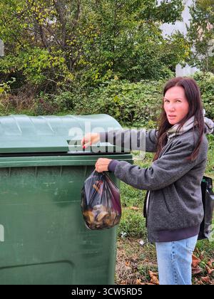 Eine Frau wirft einen Sack voller Müll in einen Mülleimer. Abfallentsorgung im Freien. Stockfoto