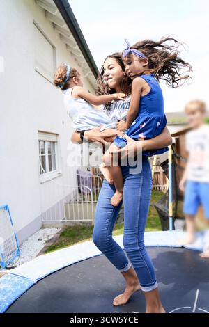 Die ältere Schwester hält Geschwister, die zu Hause auf Trampolin springen Stockfoto