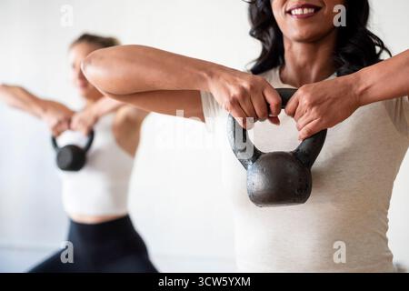 Lächelnde Frauen, die Kettlebells im Fitnessstudio heben Stockfoto