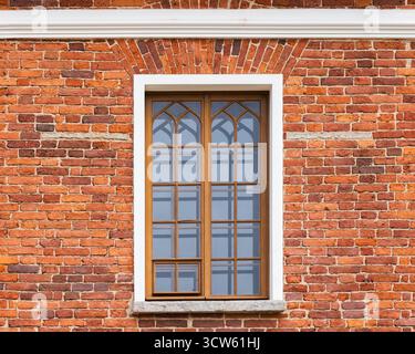 Aus nächster Nähe ein verwittertes rotes Backsteingebäude mit einem Holzfenster mit gotischen Bögen und weißen Zierleisten. Vorderansicht, Hintergrundfototex Stockfoto