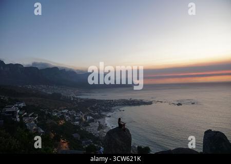 Person, die den Sonnenuntergang über Camps Bay und den zwölf Aposteln beobachtet Stockfoto