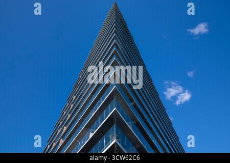 Flacher Blick auf das scharf angewinkelte Gebäude vor blauem Himmel mit kleinen flauschigen Wolken Stockfoto