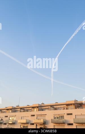 Vertikale Aufnahme von Kondensstreifen über dem modernen Dach der Stadt bei Sonnenuntergang. Konzeptbild für das Leben in der Stadt, Reisen, Klimawandel, Chemtrails-Theorie, an Stockfoto