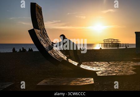 Brighton UK 9 Oktober 2025 - Besucher genießen einen wunderschönen Sonnenuntergang über Brighton Beach Passacaglia Skulptur und West Pier nach einem weiteren warmen Tag entlang der Südküste . Brighton UK 9 Oktober 2025 - Besucher genießen einen wunderschönen Sonnenuntergang über Brighton Beach Passacaglia Skulptur und West Pier nach einem weiteren warmen Tag entlang der Südküste . Passacaglia ist eine riesige, gekrümmte abstrakte Skulptur von Charles Hadcock: Credit Simon Dack / Alamy Live News : Credit Simon Dack / Alamy Live News Stockfoto