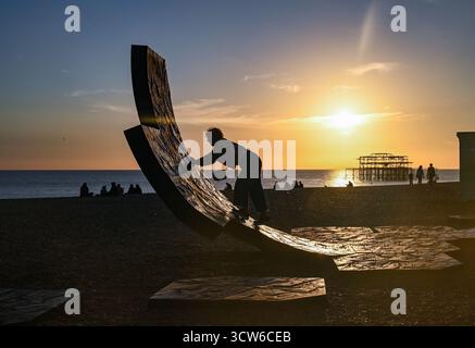 Brighton UK 9 Oktober 2025 - Besucher genießen einen wunderschönen Sonnenuntergang über Brighton Beach Passacaglia Skulptur und West Pier nach einem weiteren warmen Tag entlang der Südküste . Passacaglia ist eine riesige, gekrümmte abstrakte Skulptur von Charles Hadcock: Credit Simon Dack / Alamy Live News Stockfoto