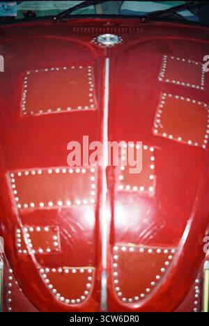Nahaufnahme einer roten VW-Käfer-Haube mit genietetem Flickwerk, aufgenommen auf analogem Film mit Blitz. Grungy Textur und starke urbane Ästhetik. Stockfoto
